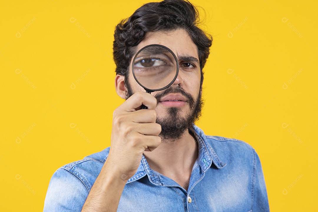 Homem jovem barbudo usando lupa sobre fundo amarelo