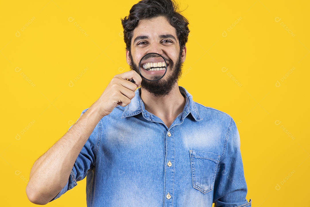 Homem jovem barbudo usando lupa sobre fundo amarelo