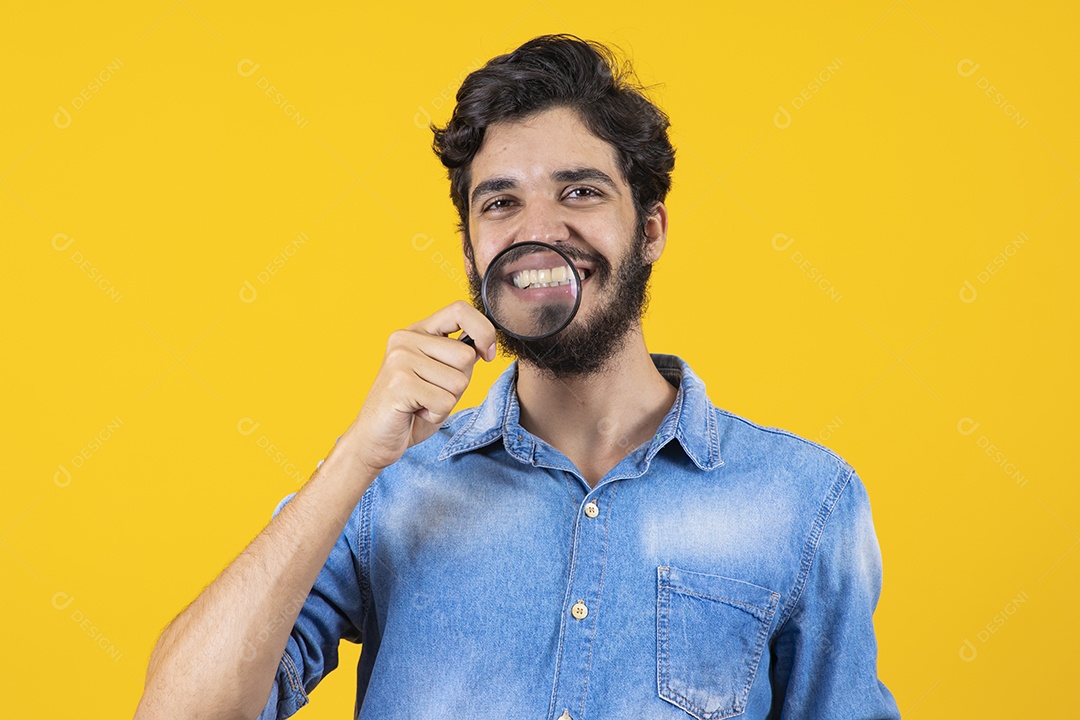 Homem jovem barbudo usando lupa sobre fundo amarelo
