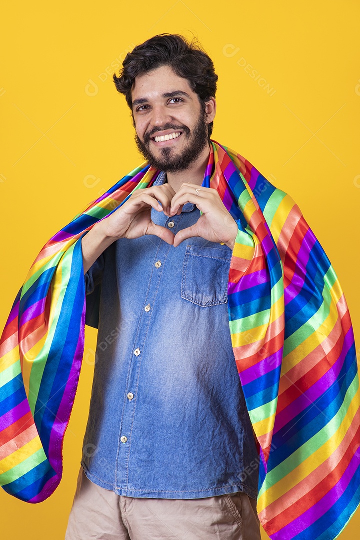 Homem jovem segurando bandeira LGBT barbudo sobre fundo amarelo