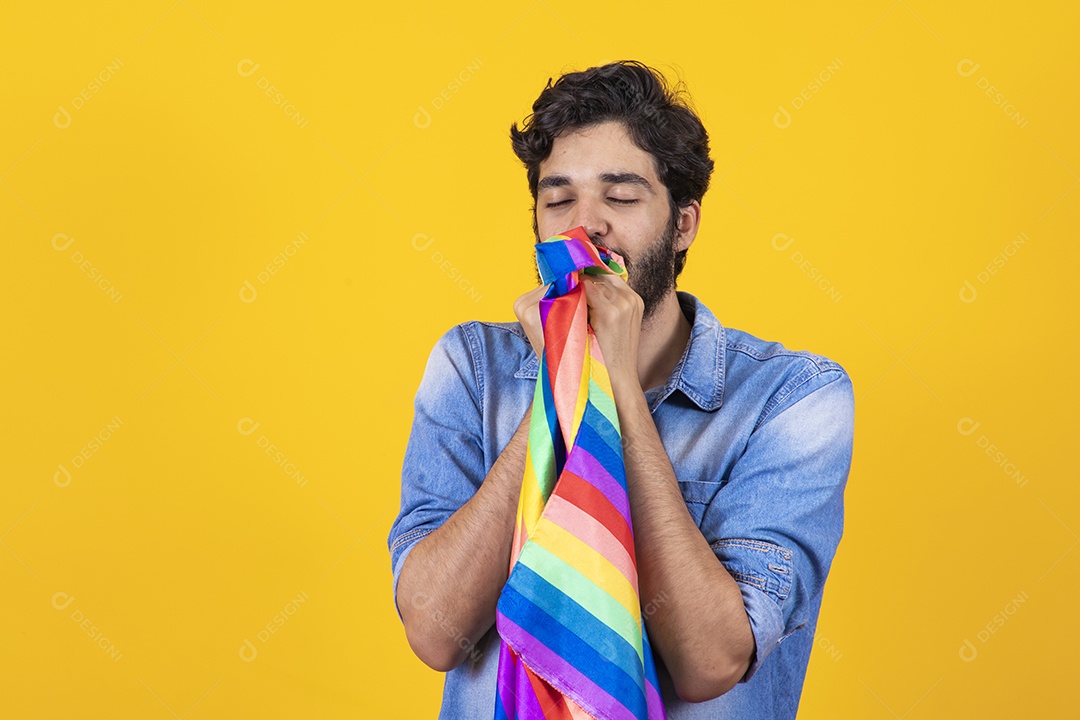 Homem jovem segurando bandeira LGBT barbudo sobre fundo amarelo