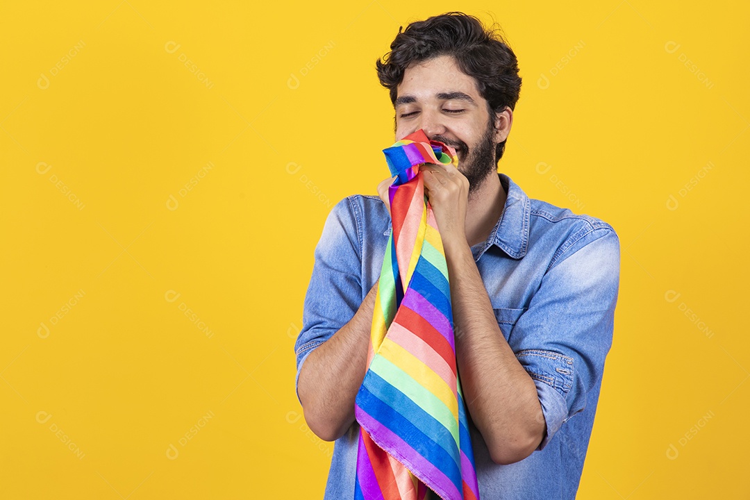 Homem jovem segurando bandeira LGBT barbudo sobre fundo amarelo