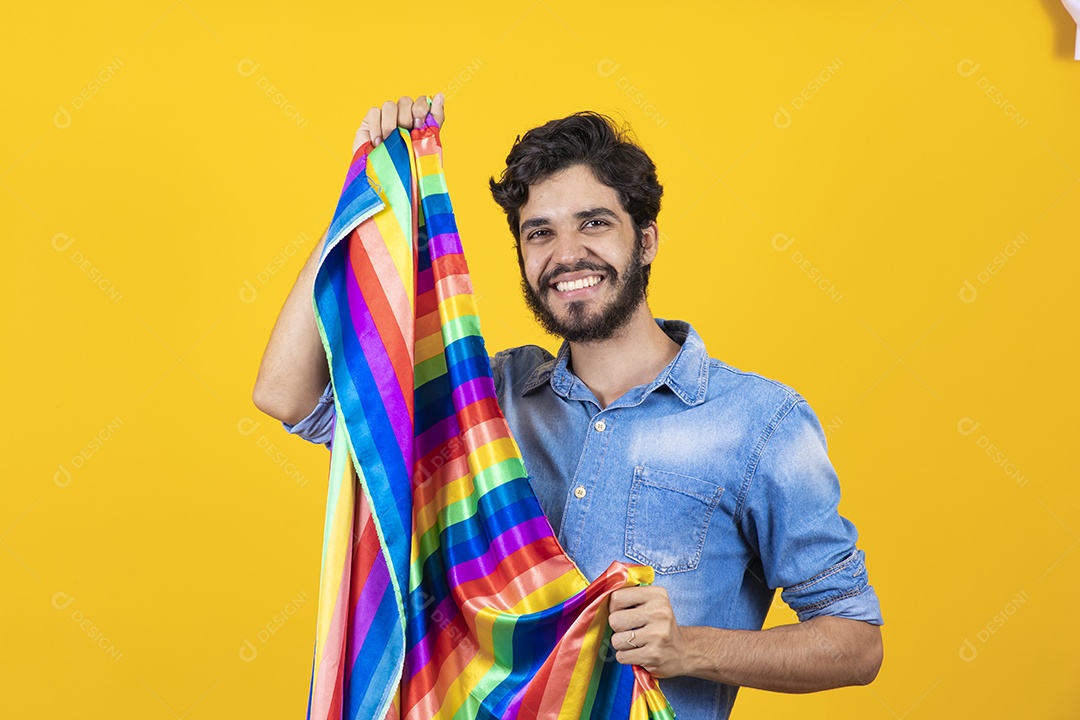 Homem jovem segurando bandeira LGBT barbudo sobre fundo amarelo