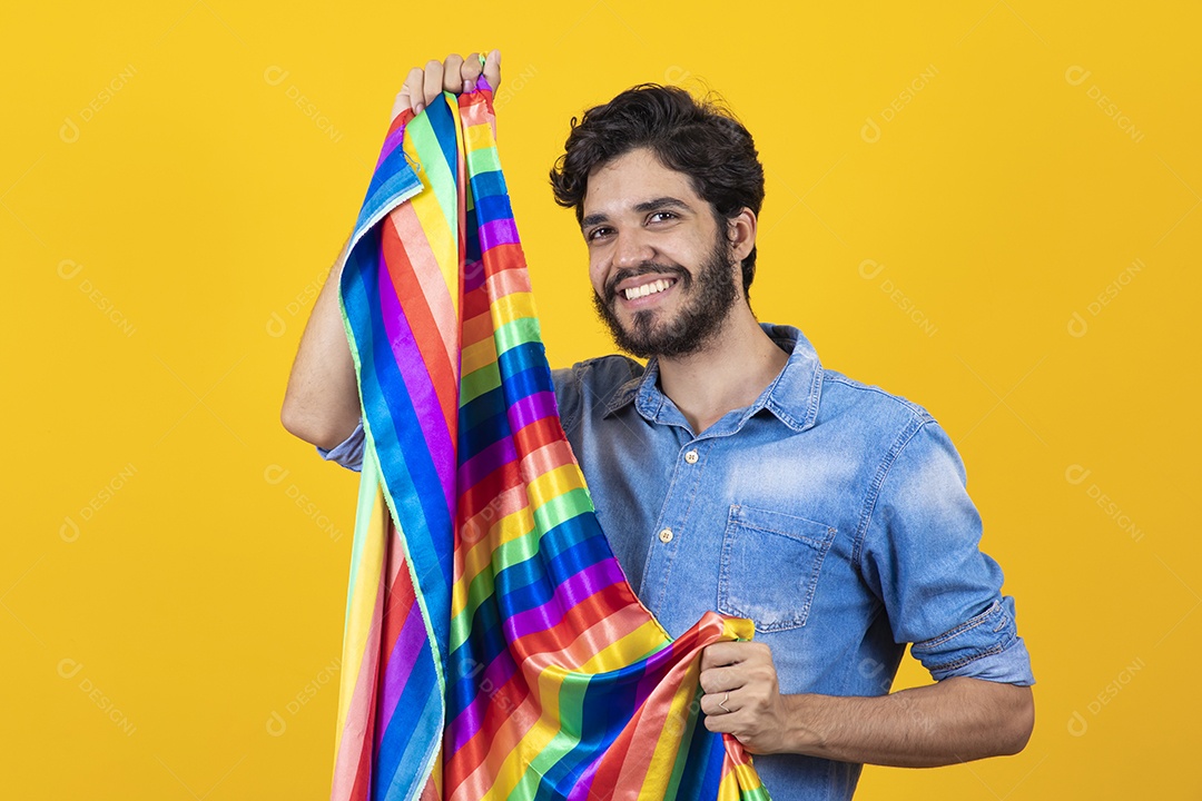 Homem jovem segurando bandeira LGBT barbudo sobre fundo amarelo