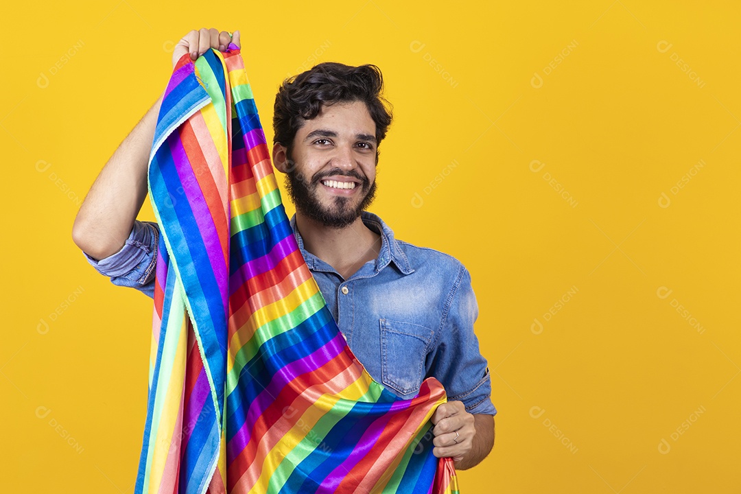 Homem jovem segurando bandeira LGBT barbudo sobre fundo amarelo