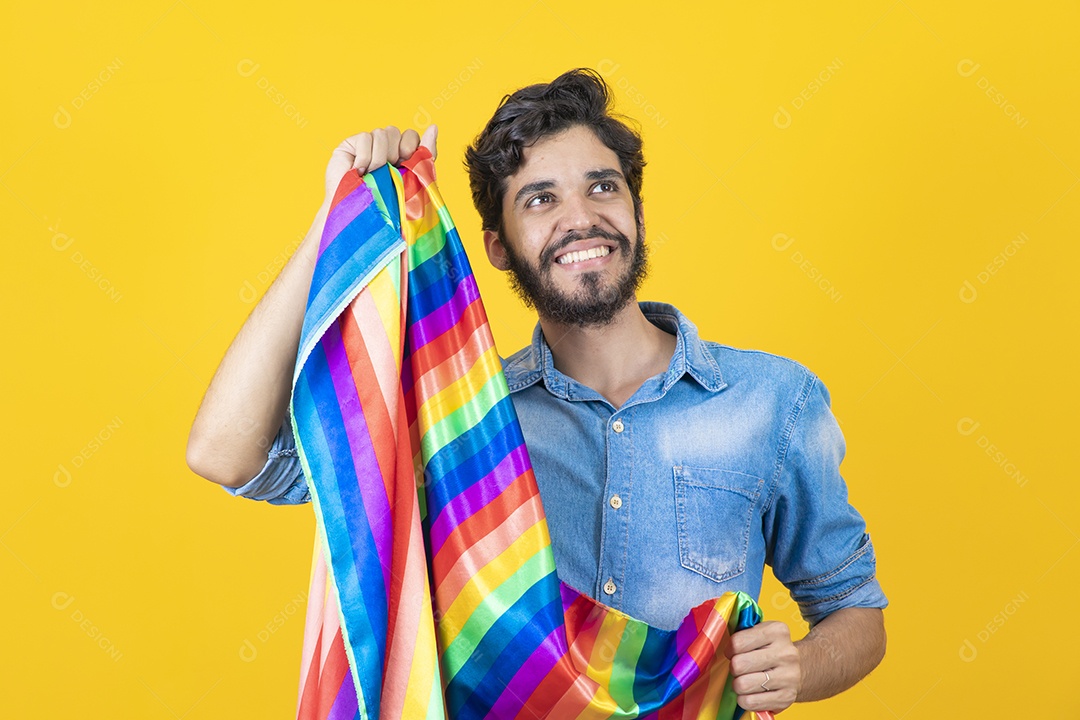 Homem jovem segurando bandeira LGBT barbudo sobre fundo amarelo