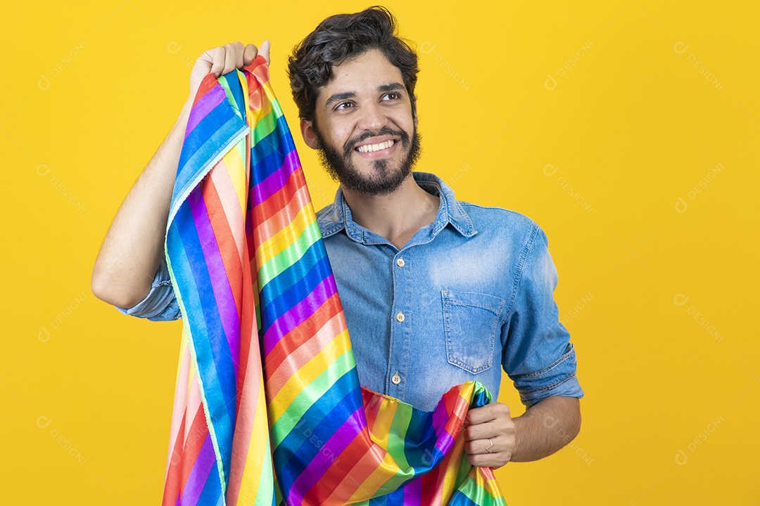 Homem jovem segurando bandeira LGBT barbudo sobre fundo amarelo