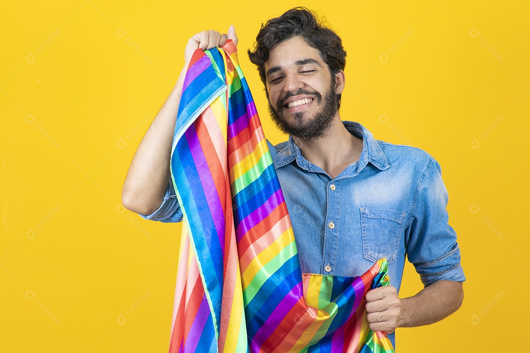 Homem jovem segurando bandeira LGBT barbudo sobre fundo amarelo