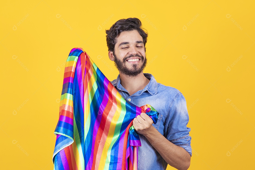 Homem jovem segurando bandeira LGBT barbudo sobre fundo amarelo