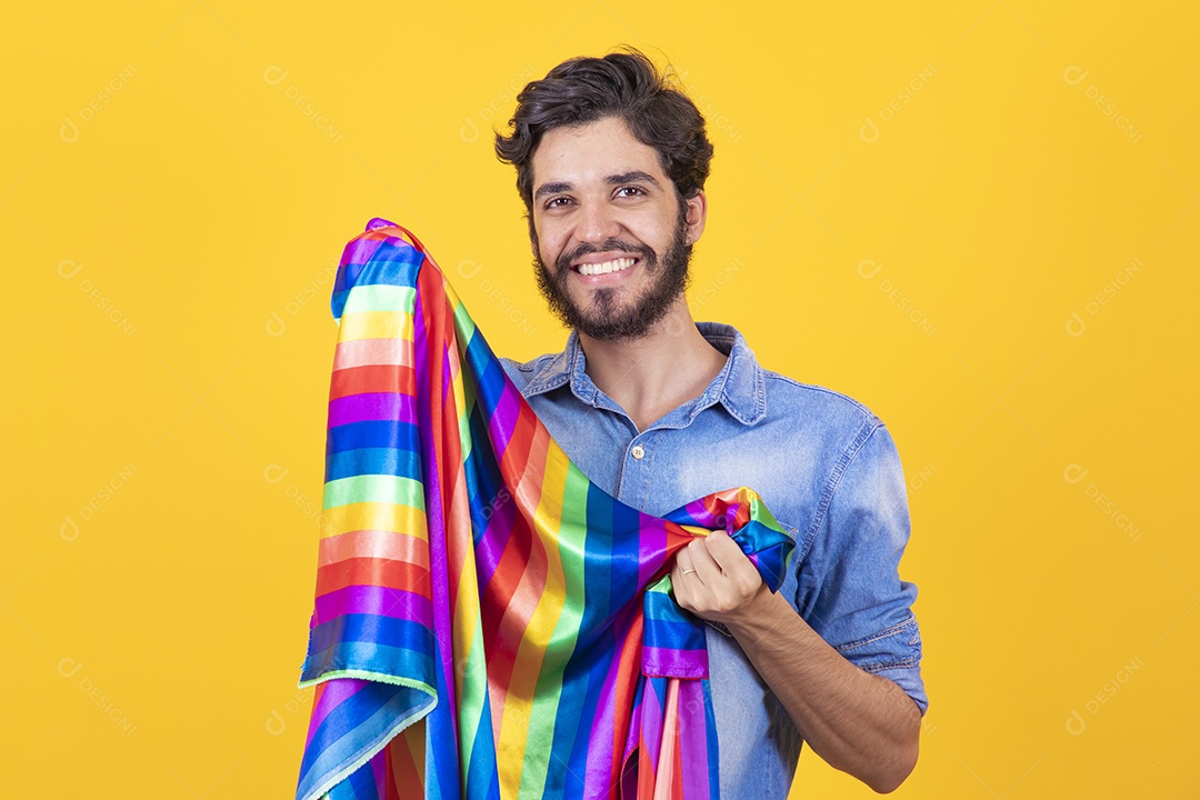 Homem jovem segurando bandeira LGBT barbudo sobre fundo amarelo