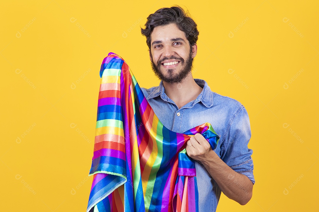 Homem jovem segurando bandeira LGBT barbudo sobre fundo amarelo