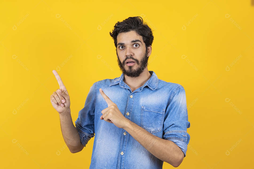 Homem jovem barbudo apontando para lado sobre fundo amarelo
