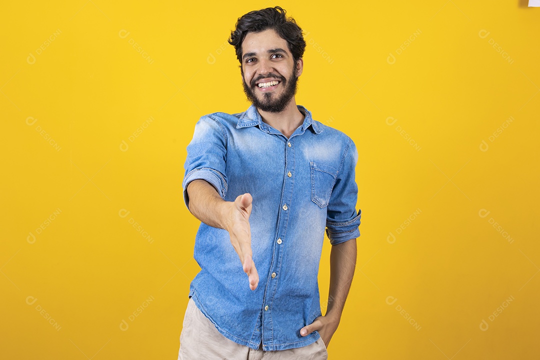 Homem jovem barbudo dando sua mão para outra pessoa aperta sobre fundo amarelo