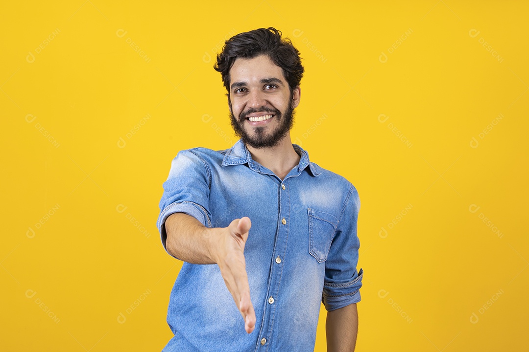 Homem jovem barbudo dando sua mão para outra pessoa aperta sobre fundo amarelo