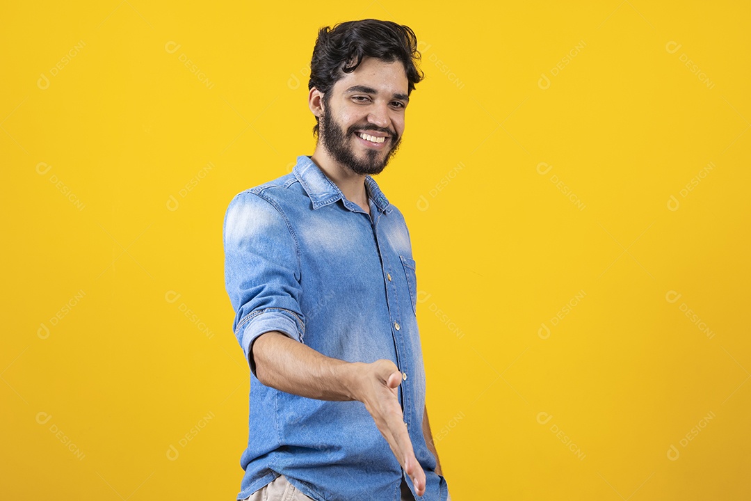 Homem jovem barbudo dando sua mão para outra pessoa aperta sobre fundo amarelo