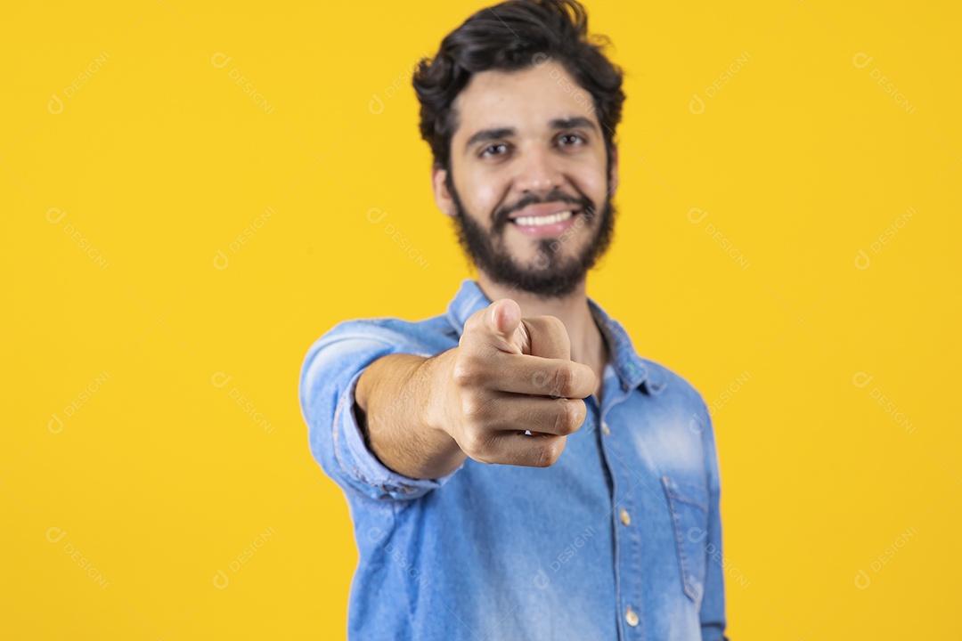 Homem jovem apontando para frente barbudo sobre fundo amarelo