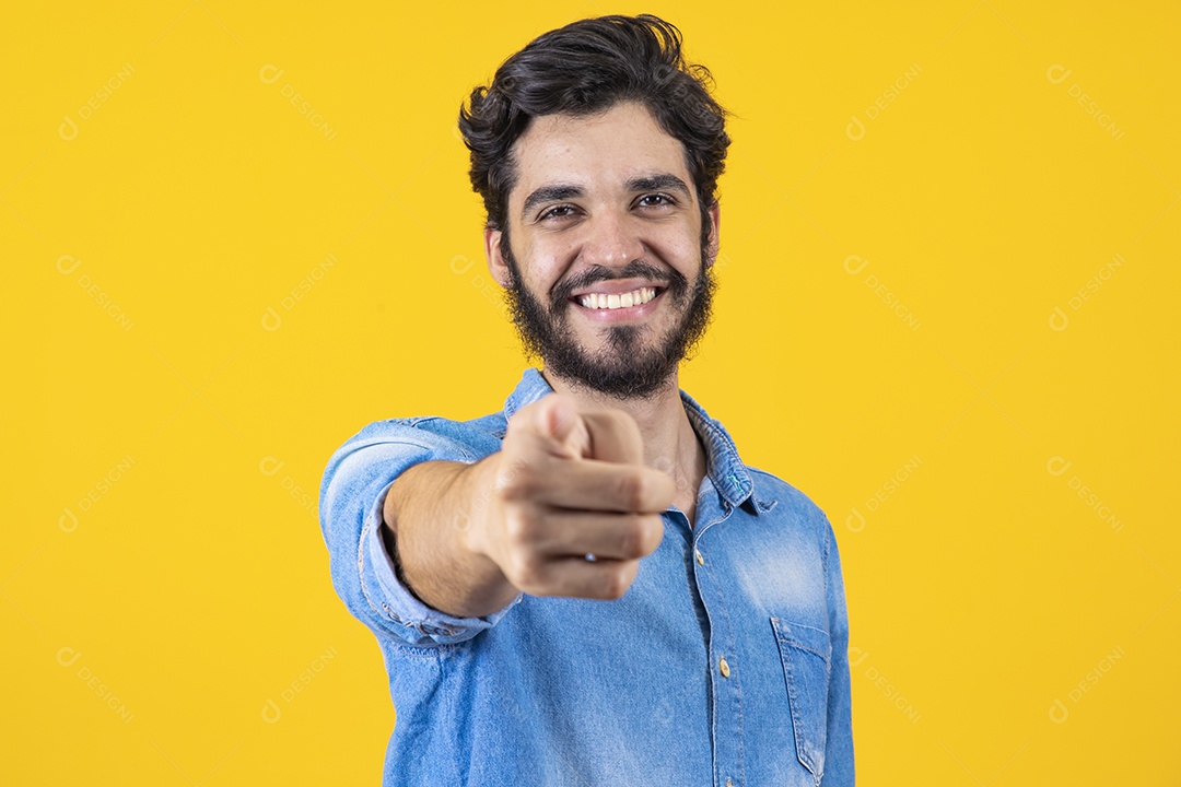 Homem jovem apontando para frente barbudo sobre fundo amarelo