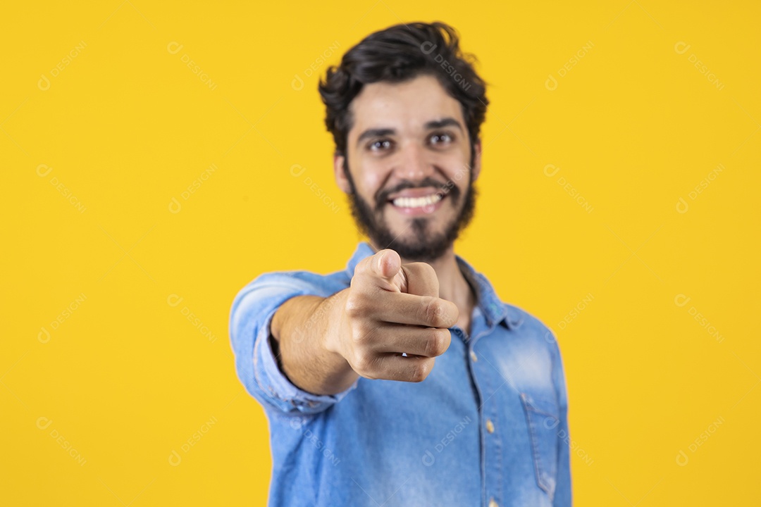 Homem jovem apontando para frente barbudo sobre fundo amarelo