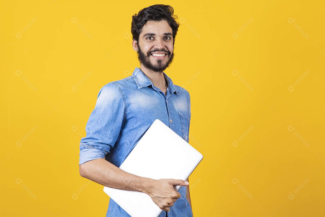 Homem jovem segurando notebook barbudo sobre fundo amarelo