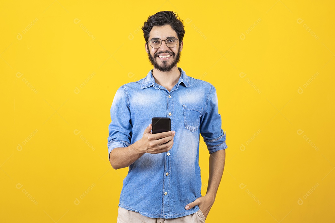 Homem jovem segurando celular barbudo sobre fundo amarelo
