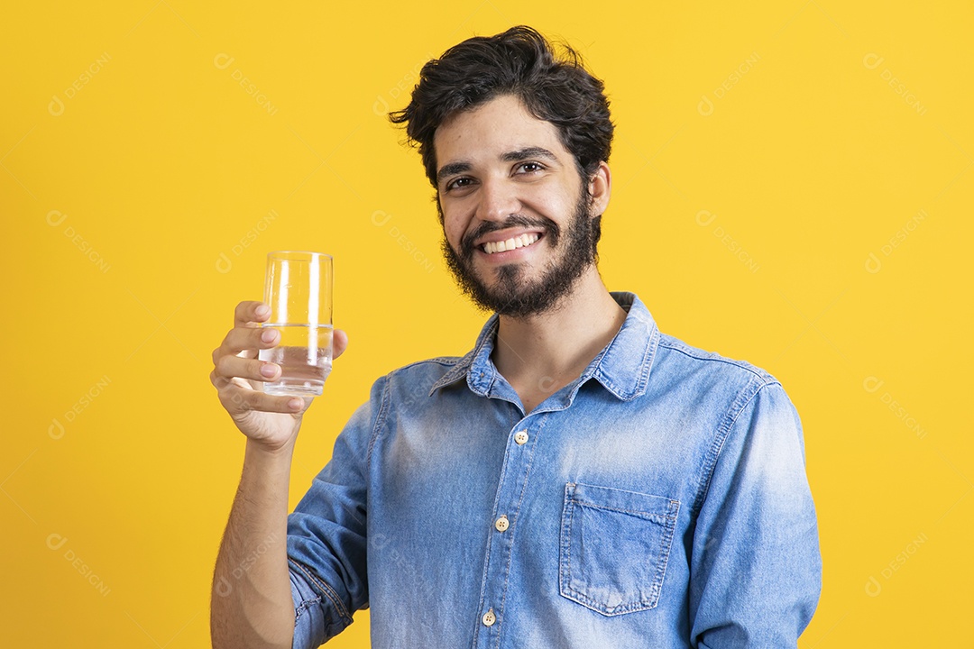 Homem jovem segurando copo de vidro barbudo sobre fundo amarelo