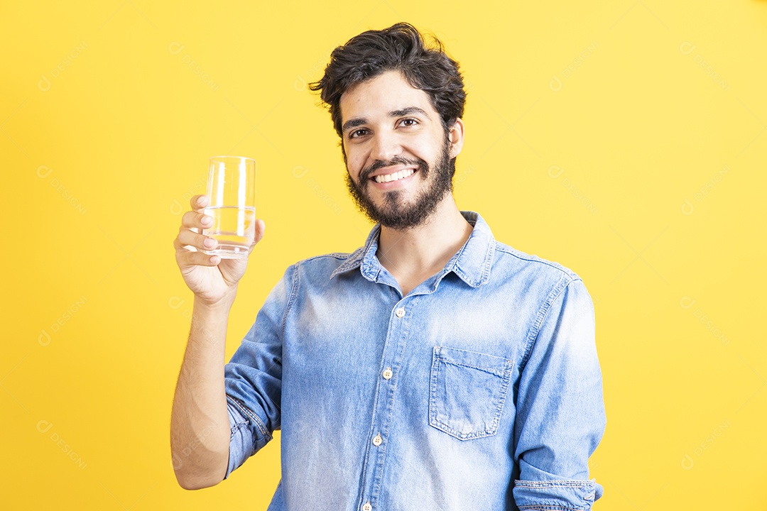 Homem jovem segurando copo de vidro barbudo sobre fundo amarelo