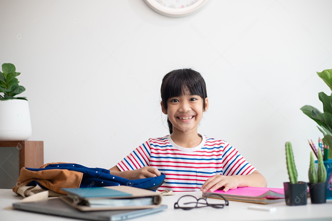 Menina asiática bonita da escola primária arrumando suas mochilas escolares, preparando-se para o primeiro dia de aula