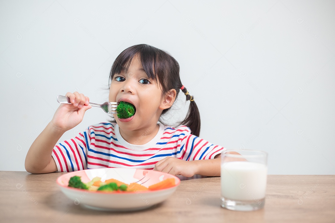 Menina asiática bonita comendo vegetais saudáveis ​​e leite para sua refeição