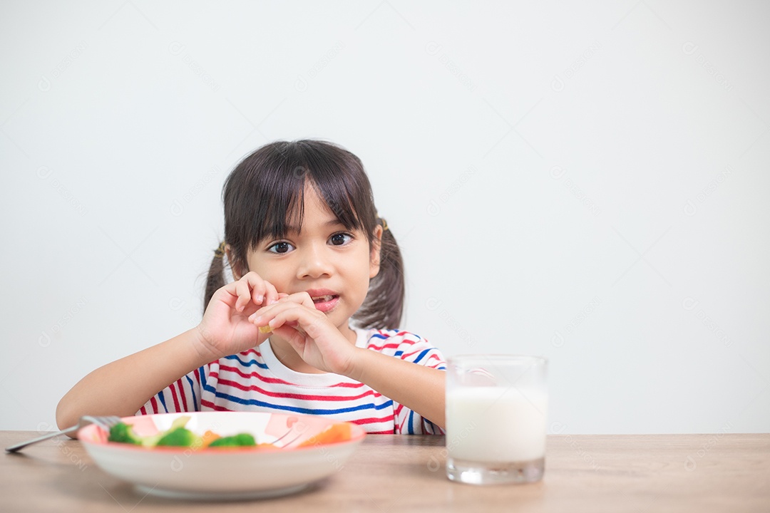 Menina asiática bonita comendo vegetais saudáveis ​​e leite para sua refeição