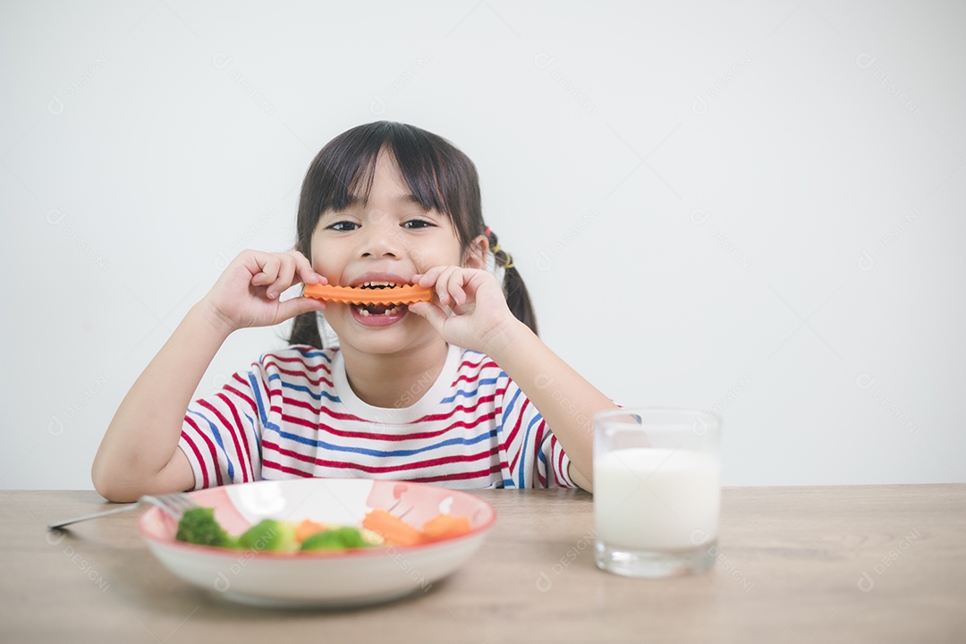 Menina asiática bonita comendo vegetais saudáveis ​​e leite para sua refeição