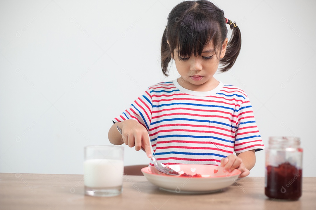 Menina asiática tomando café da manhã com pão e geléia com um copo de leite