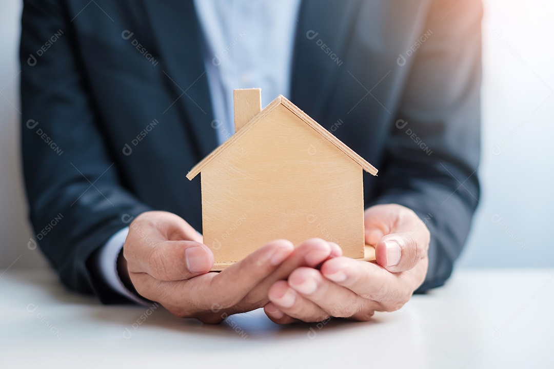 Mão de empresário segurando o modelo de casa de madeira. Imobiliário, compra e venda, seguro de propriedade, conceitos de contrato de aluguel e contrato