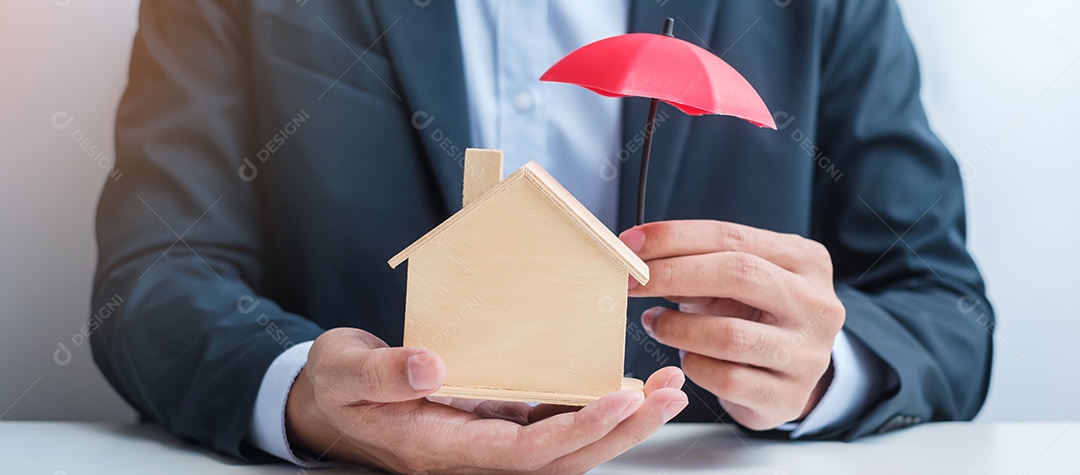 Mão de empresário segurando um guarda-chuva vermelho modelo de casa de madeira. conceitos imobiliários, seguros e imobiliários