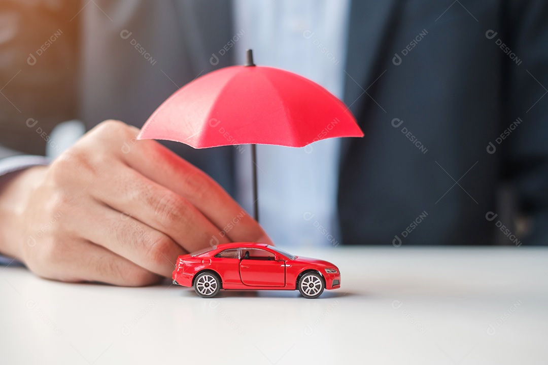 Mão de empresário segurando o guarda-chuva e cobrir o brinquedo do carro vermelho na mesa. Seguro automóvel, garantia, reparação, financeiro, bancário e conceito de dinheiro