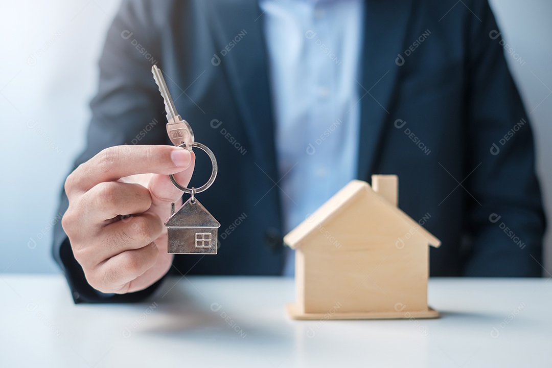 Mão de empresário segurando a chave com modelo de madeira para casa. Imobiliário, compra e venda, seguro de propriedade, conceitos de contrato de aluguel e contrato