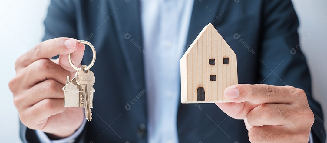 Mão de empresário segurando a chave com modelo de madeira para casa. Imobiliário, compra e venda, seguro de propriedade, conceitos de contrato de aluguel e contrato