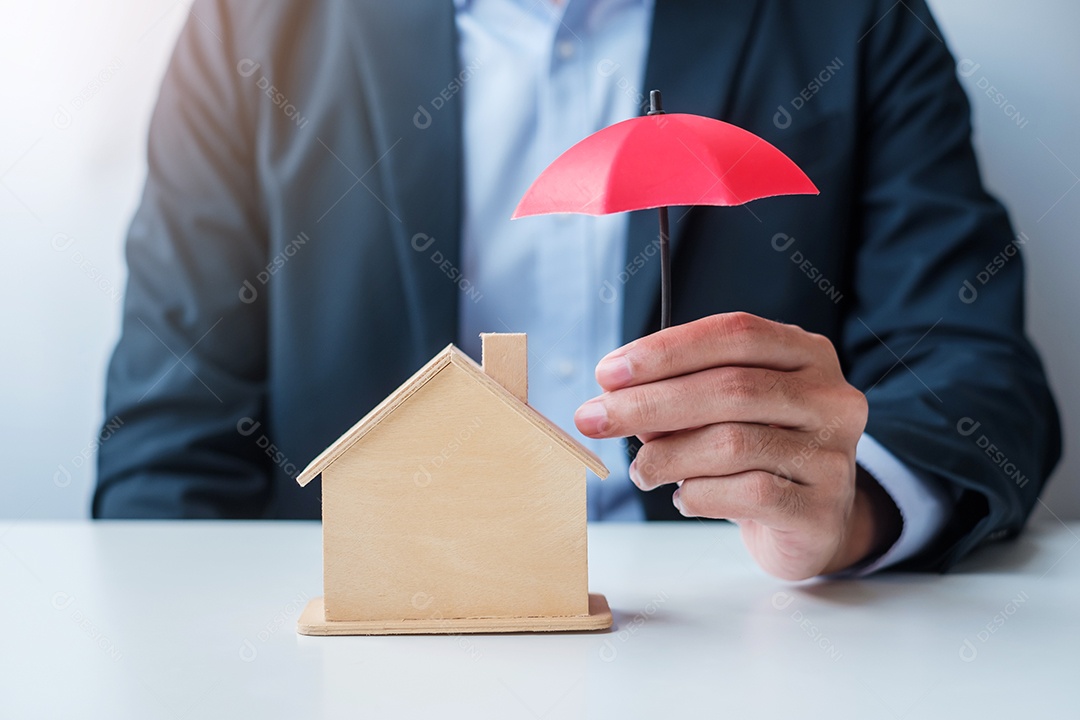 Mão de empresário segurando um guarda-chuva vermelho modelo de casa de madeira. conceitos imobiliários, seguros e imobiliários