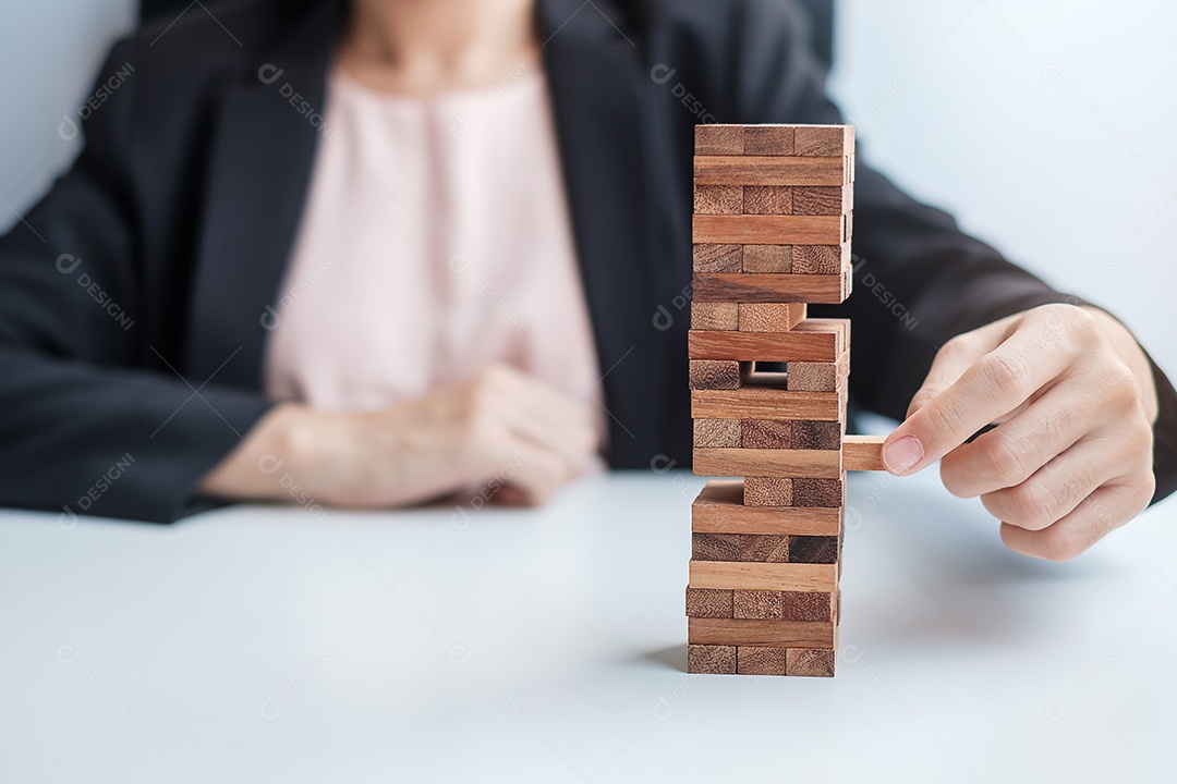 Mão de empresária colocando ou puxando o bloco de madeira na torre. Conceitos de planejamento de negócios, gerenciamento de riscos, solução e estratégia