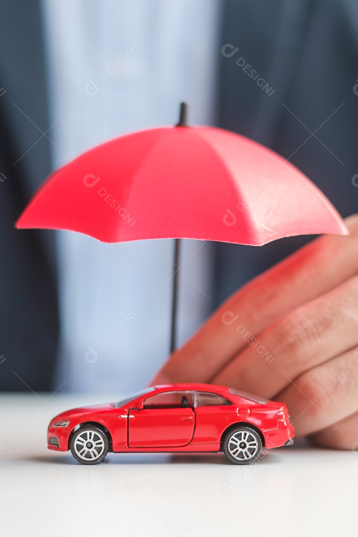 Mão de empresário segurando o guarda-chuva e cobrir o brinquedo do carro vermelho na mesa. Seguro automóvel, garantia, reparação, financeiro, bancário e conceito de dinheiro