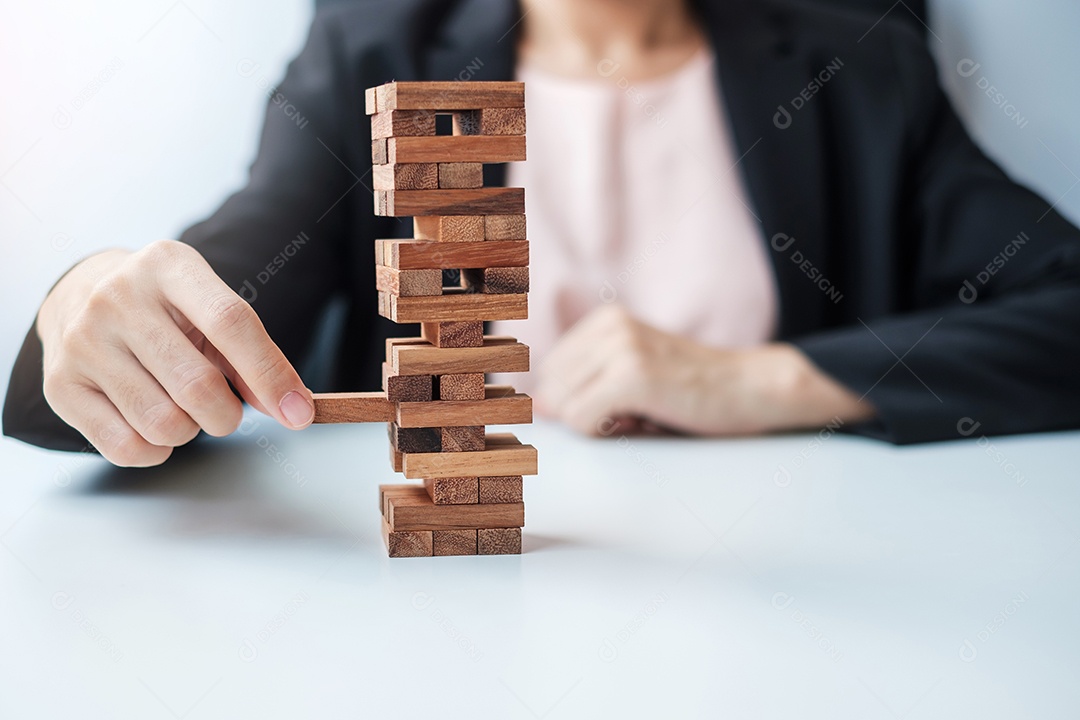 Businesswoman hand placing or pulling wooden block on tower. Business planning, risk management, solution and strategy concepts
