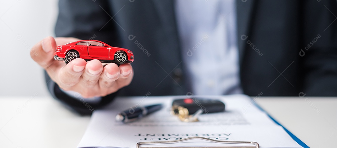 Mão de empresário segurando o brinquedo do carro vermelho com veículo sem chave, caneta e documento de contrato. conceitos de compra e venda, seguro, aluguel e contrato