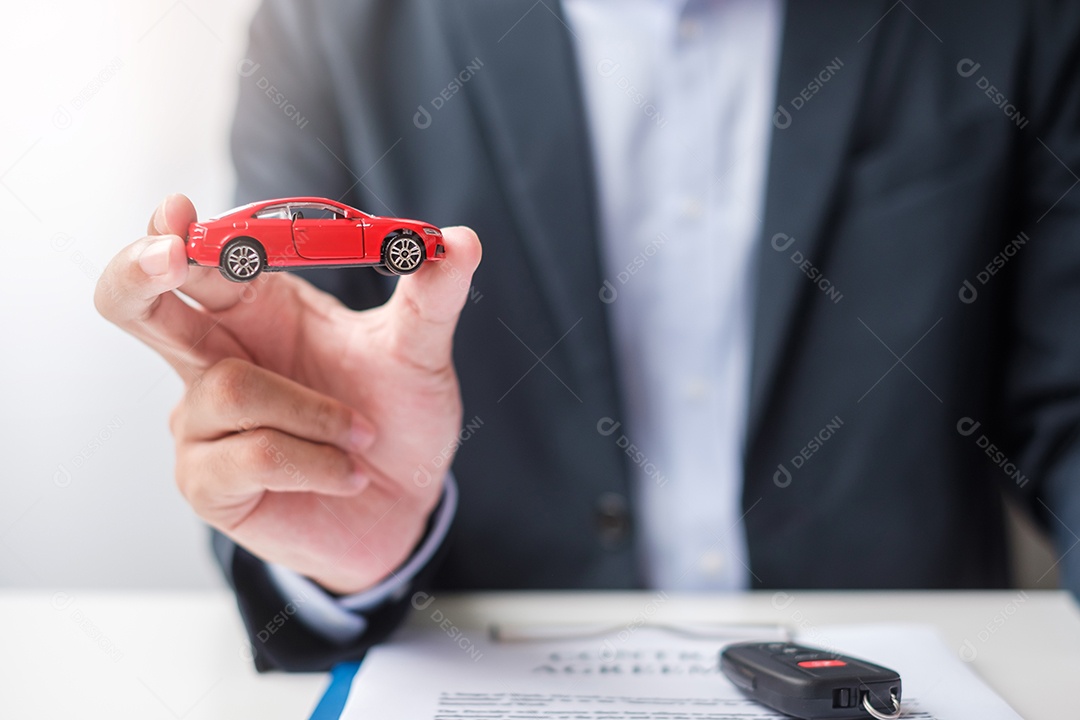 Mão de empresário segurando o brinquedo do carro vermelho com veículo sem chave, caneta e documento de contrato. conceitos de compra e venda, seguro, aluguel e contrato