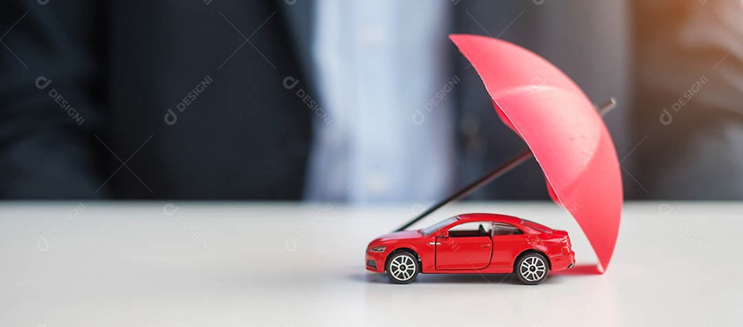 Mão de empresário segurando o guarda-chuva e cobrir o brinquedo do carro vermelho na mesa. Seguro automóvel, garantia, reparação, financeiro, bancário e conceito de dinheiro