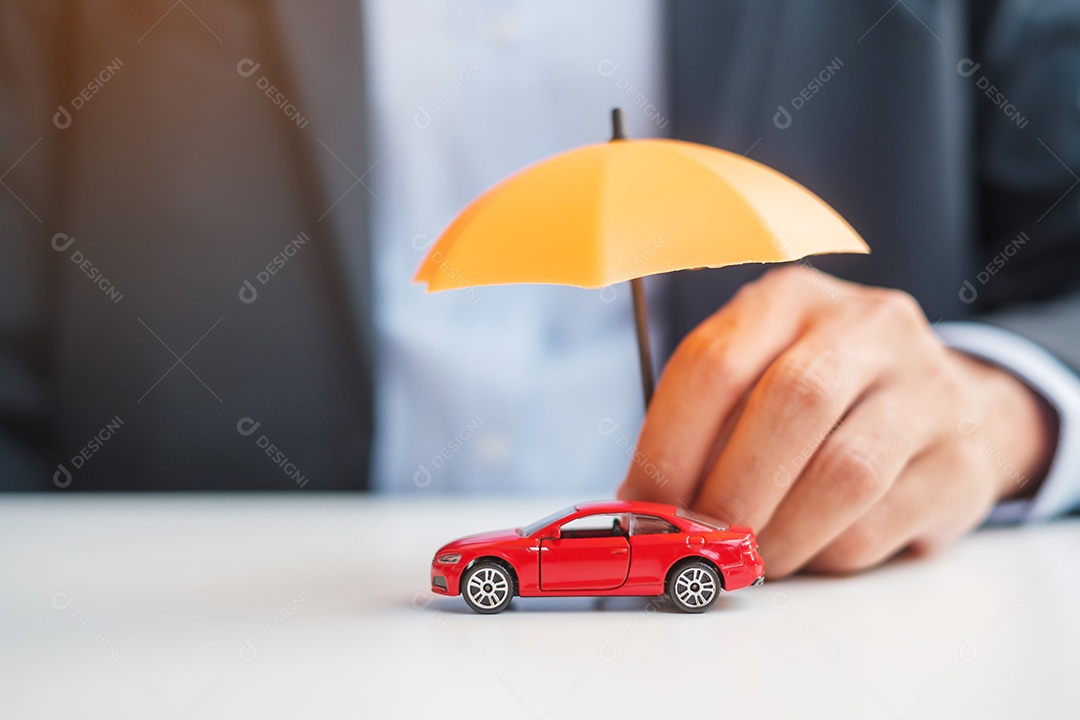 Mão de empresário segurando o guarda-chuva e cobrir o brinquedo do carro vermelho na mesa. Seguro automóvel, garantia, reparação, financeiro, bancário e conceito de dinheiro