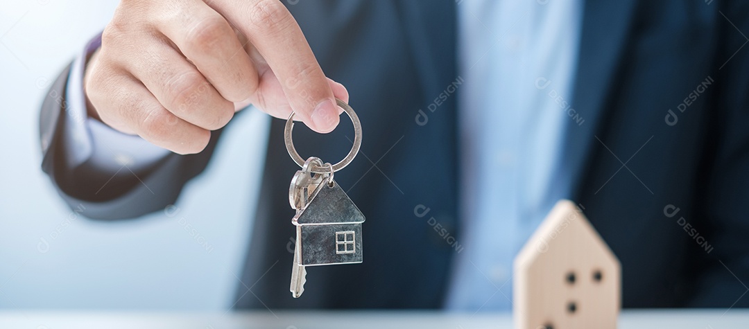 Mão de empresário segurando a chave com modelo de madeira para casa. Imobiliário, compra e venda, seguro de propriedade, conceitos de contrato de aluguel e contrato