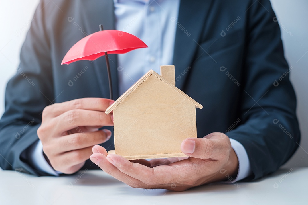 Mão de empresário segurando um guarda-chuva vermelho modelo de casa de madeira. conceitos imobiliários, seguros e imobiliários