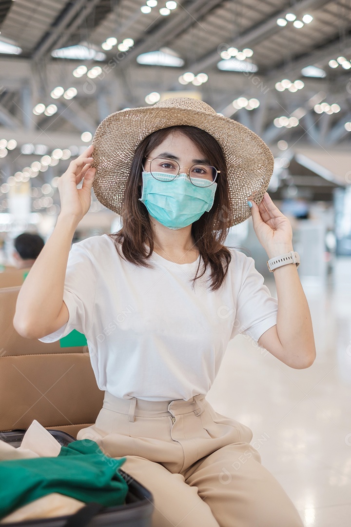 Jovem mulher usando máscara facial com bagagem andando no aeroporto, proteção contra infecção por doença de coronavírus