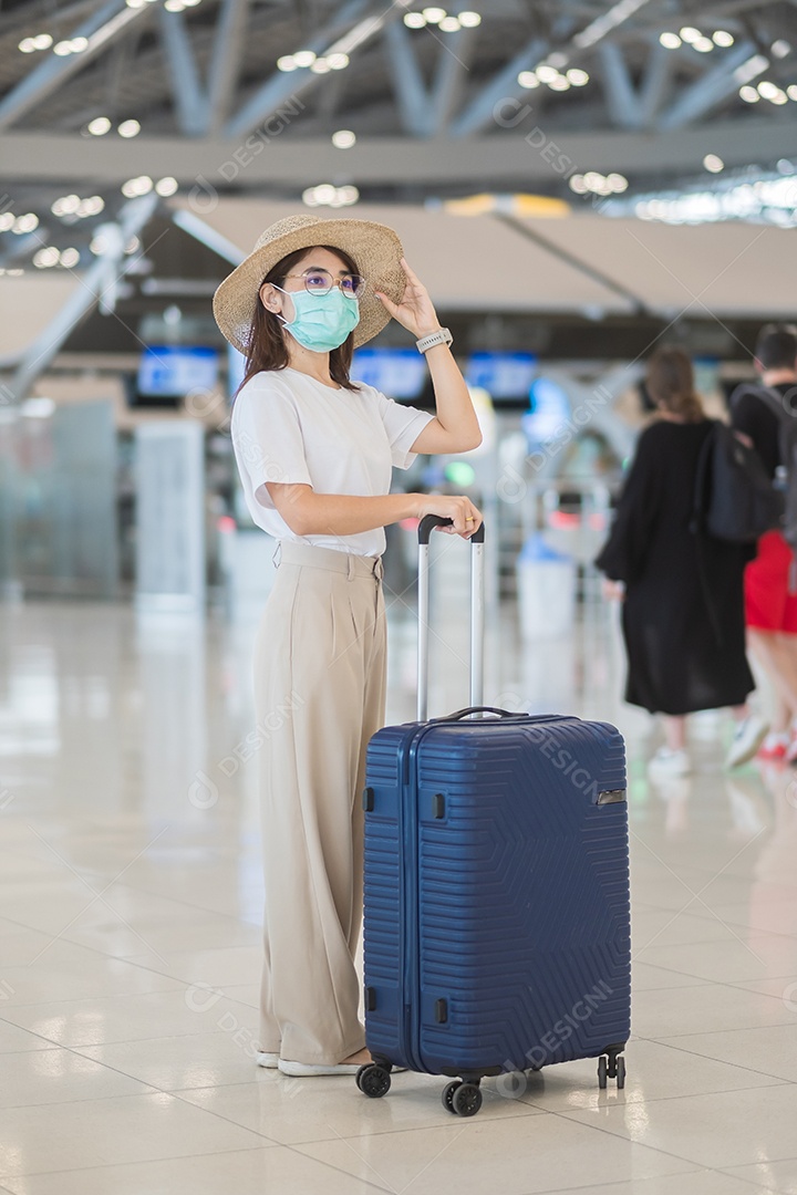 Jovem mulher usando máscara facial com bagagem andando no aeroporto, proteção contra infecção por doença de coronavírus