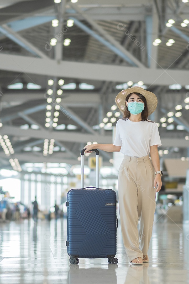 Jovem mulher usando máscara facial com bagagem andando no aeroporto, proteção contra infecção por doença de coronavírus