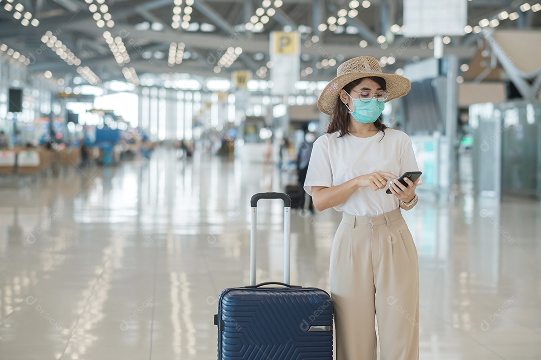 Mulher turista asiática usando máscara facial e usando smartphone móvel no aeroporto, proteção contra infecção por doença de Coronavirus